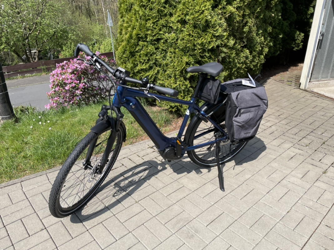 Dark blue electric bike with panniers in front of a garage.
